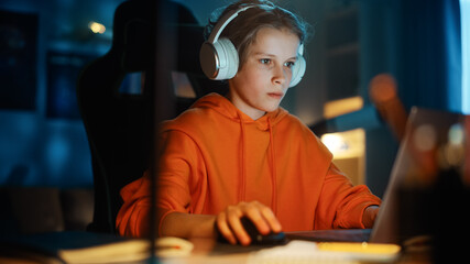 Excited Young Boy in Headphones Playing Video Games on Laptop Computer in Cozy Dark Room at Home....