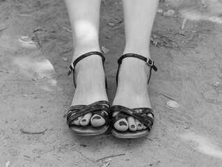 Beautiful legs of a girl in black sandals and toes with a pedicure. Closeup of feet with painted nails in black sandals. Black and white photo.