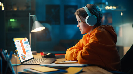 Smart Young Boy in Headphones Researching Homework Topic from an Exercise Book on Laptop Computer. Happy Teenager Browsing Educational Research, Writing in Notebook, Studying School Material.
