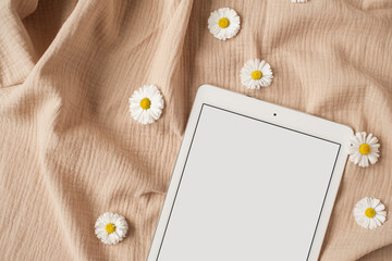 Flatlay of blank screen tablet pad, chamomile flower buds neutral beige muslin cloth. Aesthetic...