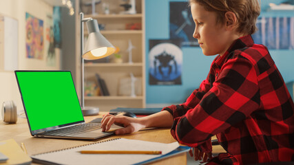 Smart Young Boy Researching Homework on Laptop Computer with Green Chroma Key Screen Display Mock Up. Teenager Browsing Educational Research, Chatting on Social Media, Studying School Material.
