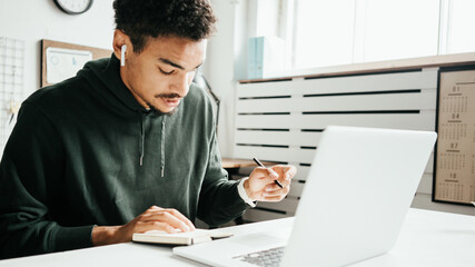 Investing in stock exchange market. Black man trading remote using laptop. Writing down key points