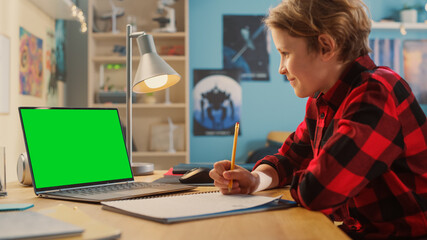 Smart Young Boy Attending Online Class on Laptop Computer with Green Screen at Home. Happy Teenager Browsing Educational Research Online, Writing in Notebook, Studying School Homework.