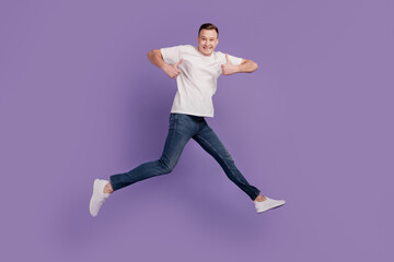 Portrait of funky sportive guy jump run raise thumbs up on purple background