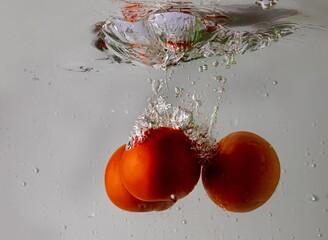 Ripe tomato falls deeply under water with a big splash