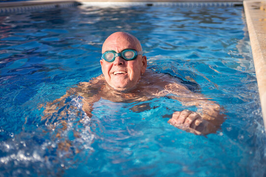 Old smiling man in goggles swimming in pool