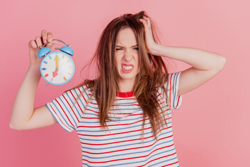 Portrait of messy hairstyle mad lady hold alarm clock timer tear hair on pink background