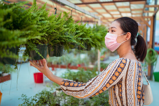 Asian shopper in disposable mask picking fern in garden shop