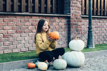 Funny child girl in orange pullover for Halloween with pumpkin and on a dark brick background.