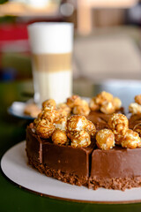 Chocolate cake with cream cheese glaze and caramel pop corn topping served with a glass of latte coffee in cafe