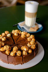 Chocolate cake with cream cheese glaze and caramel pop corn topping served with a glass of latte coffee in cafe