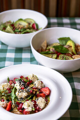 Three plates of healthy salad, green salad with cucumber, zucchini and strawberries in white bowl.