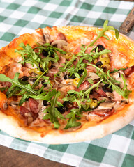Delicious Italian pizza served on wooden table with green plaid tablecloth, traditional recipe.