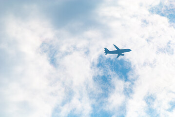 the silhouette of a passenger airliner in the blue sky behind the clouds