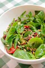 Spinach salad with tomatoes, fresh arugula, pumpkin seeds, pomegranate seeds served in a white bowl