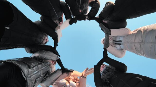 Friends on a winter day join their hands with mittens in a circle.