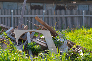 construction of a dacha: a large pile of unnecessary construction debris and sawn boards overgrown with grass against the background of a wooden fence