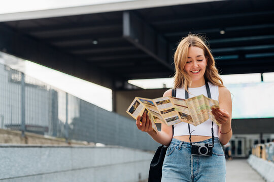 Young caucasian woman traveller holding tourist map smiling discovering and sightseeing