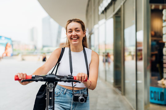Young caucasian smiling woman outdoor riding kick scooter enjoying green living and sustainability