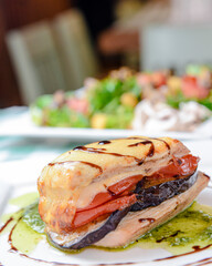 Rosemary chicken with oven-roasted ratatouille served on a white square plate over table with green...