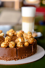 Chocolate cake with cream cheese glaze and caramel pop corn topping served with a glass of latte coffee in cafe