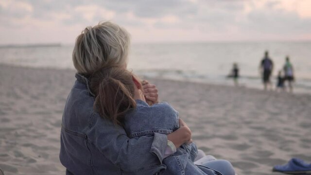 Mom hugs the daughter of a teenager by the sea at sunset.