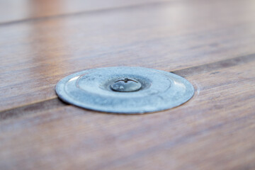 Metal bolt with nut and washer in a wooden table. Screw with a Phillips screwdriver head screwed into the worktop.