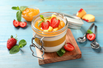 Delicious panna cotta with mango coulis and fresh fruit pieces on light blue wooden table