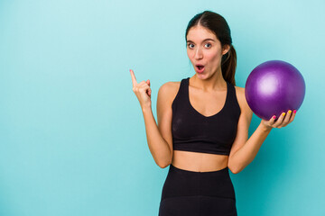 Young caucasian fitness woman holding a ball isolated on blue background pointing to the side