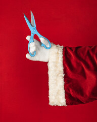 Close-up of the right hand of Santa Claus in traditional costume holding blue scissors.