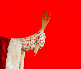 Santa Claus's hand in a kitchen glove holds a wooden fork. Santa claus preparing a festive christmas dinner