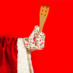 Santa Claus's hand in a kitchen glove holds a wooden spatula. Santa claus preparing a festive christmas dinner.