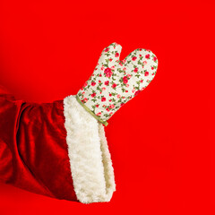 Santa Claus's hand in a kitchen glove holds a wooden fork. Santa claus preparing a festive christmas dinner.