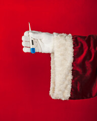Santa's Hand holding  thermometer on bright red background. Winter holiday, vacation booking concept.