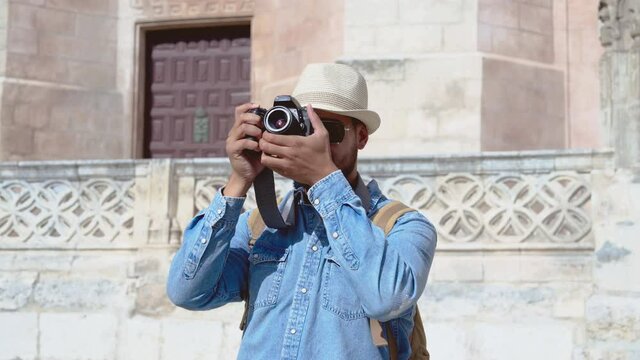 Young handsome stylish male photographer taking pictures with photo camera outdoor in old town. Cheerful man making photos of town urban architecture. High quality 4k footage