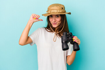 Young caucasian explorer woman holding binoculars isolated on blue background feels proud and self confident, example to follow.