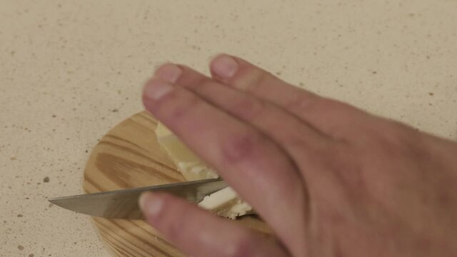 Galician tetilla cheese is cut with a knife by a woman's hands in a kitchen.