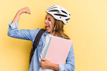 Young caucasian student woman wearing a bike helmet isolated on yellow background  raising fist after a victory, winner concept.