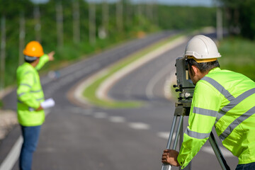 Picture of two civil engineers using theodolites measuring land coordinates standing at outdoor theodolites at a road construction site.