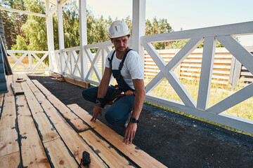 Builder squatting and pressing floorboard to porch ground