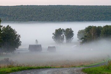 sunrise, fog covered the river valley,  rural buildings are visible through the fog