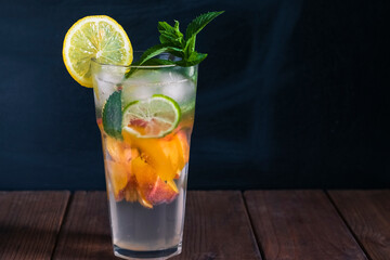 Peach mojito in a transparent glass with ice, on a dark background