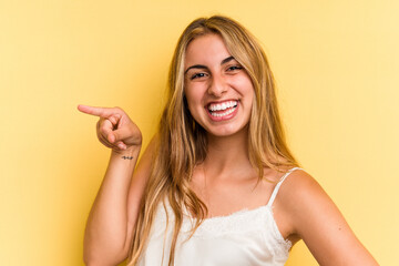 Young caucasian blonde woman isolated on yellow background  smiling cheerfully pointing with forefinger away.