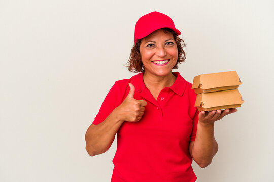 Middle age delivery woman taking burguers isolated on white background smiling and raising thumb up