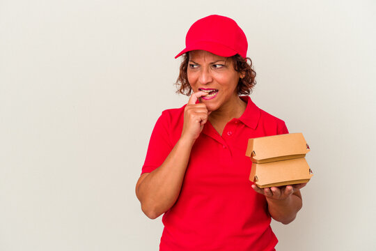 Middle age delivery woman taking burguers isolated on white background relaxed thinking about something looking at a copy space.