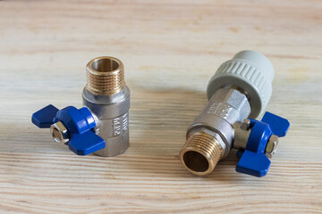 Two ball, half-inch metal valves with an adapter for a polypropylene pipe, close-up, on a wooden...