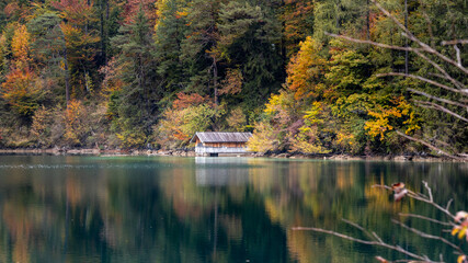 Boathouse and trees with autumn colors reflecting in the lake 
