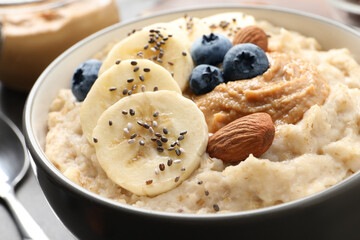 Tasty oatmeal porridge with toppings in bowl on table, closeup