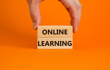 Online learning symbol. Concept words 'Online learning' on wooden blocks on a beautiful orange background. Businessman hand. Business, educational and online learning concept, copy space.
