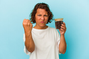 Middle age latin woman holding a coffee jar isolated on blue background showing fist to camera, aggressive facial expression.